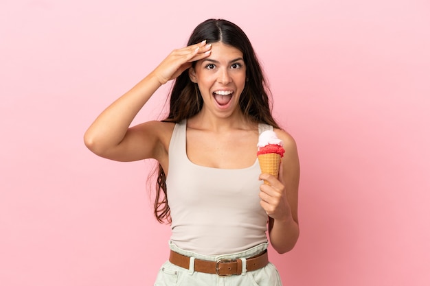 Giovane donna caucasica con un gelato alla cornetta isolato su sfondo rosa con espressione a sorpresa
