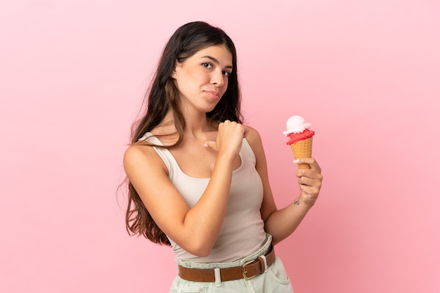 Giovane donna caucasica con un gelato alla cornetta isolato su sfondo rosa orgoglioso e soddisfatto di sé