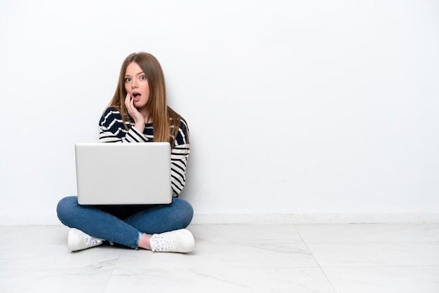 Giovane donna caucasica con un laptop seduto sul pavimento isolato su sfondo bianco sorpreso e scioccato mentre guarda a destra