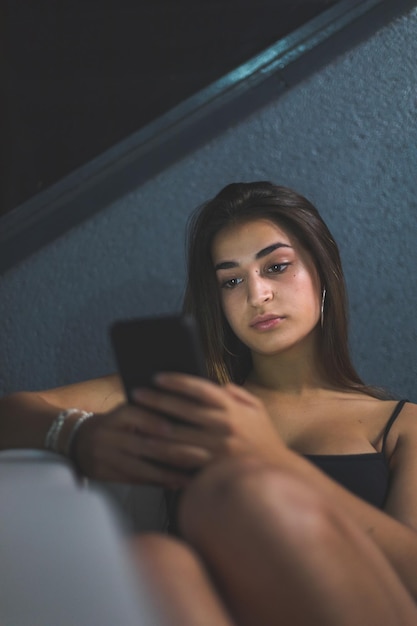 Giovane donna caucasica con un telefono cellulare sul divano della terrazza di notte. Madrid, Spagna.