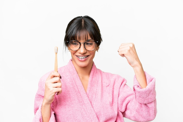 Giovane donna caucasica con uno spazzolino da denti su uno sfondo bianco isolato che celebra una vittoria