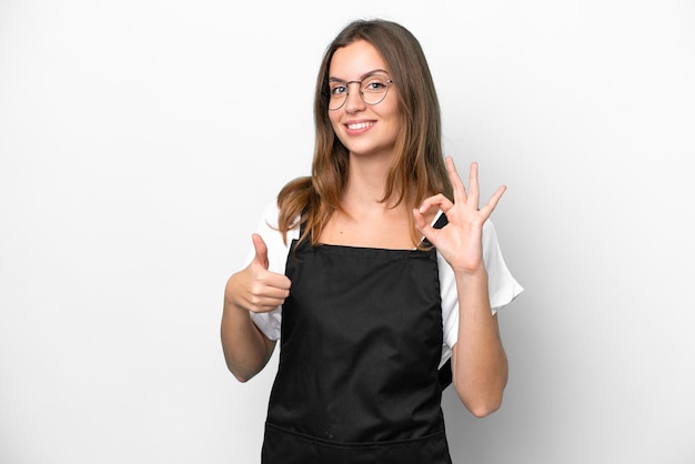 Giovane donna caucasica del cameriere del ristorante isolata su sfondo bianco che mostra il segno giusto e il gesto del pollice in su