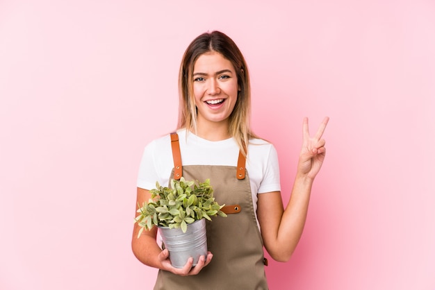 Giovane donna caucasica del giardiniere in una parete rosa allegra e spensierata che mostra un simbolo di pace con le dita.