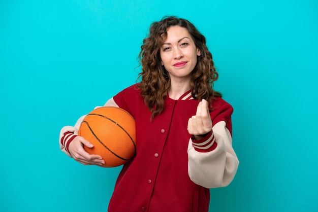 Giovane donna caucasica del giocatore di basket isolata su sfondo blu che fa gesto di denaro