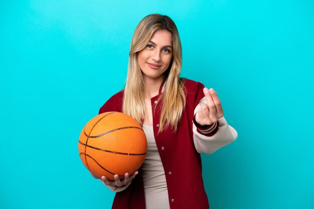 Giovane donna caucasica del giocatore di basket isolata su sfondo blu che fa gesto di denaro