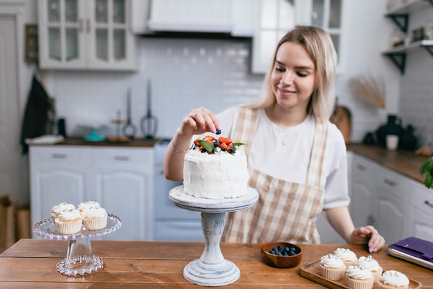 Giovane donna caucasica del pasticcere pasticcere con la torta sul tavolo della cucina