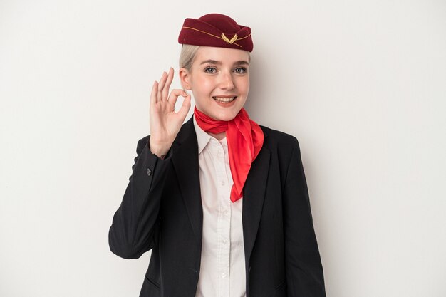 Giovane donna caucasica dell'assistente di volo isolata su fondo bianco allegro e sicuro che mostra gesto giusto.