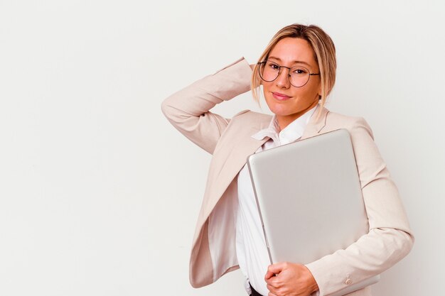 Giovane donna caucasica di affari che tiene un computer portatile isolato su priorità bassa bianca che tocca la parte posteriore della testa, pensando e facendo una scelta.