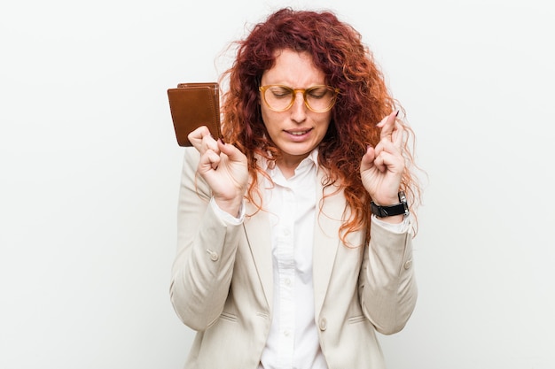 Giovane donna caucasica di redhead che tiene le dita di un incrocio del portafoglio per avere fortuna