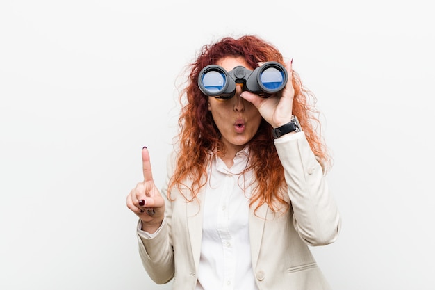 Giovane donna caucasica di redhead di affari che tiene un binocolo che ha una grande idea