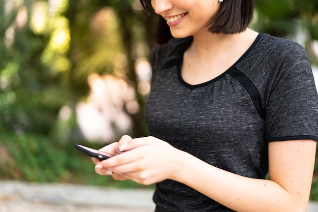 Giovane donna caucasica di sport che invia un messaggio o un'e-mail con il cellulare all'aperto in un parco