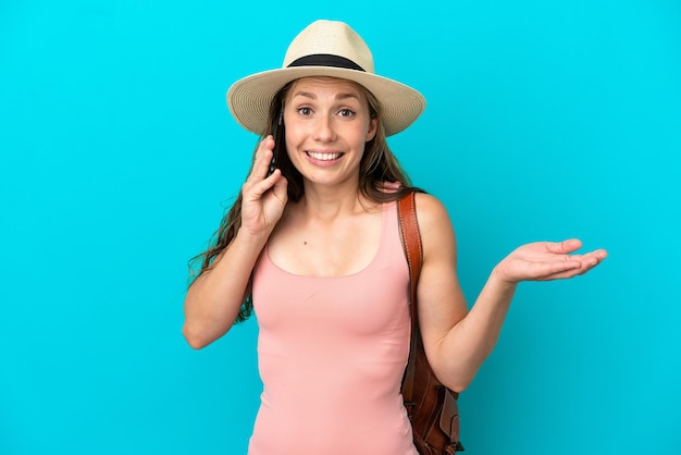 Giovane donna caucasica durante le vacanze estive isolata su sfondo blu mantenendo una conversazione con il telefono cellulare con qualcuno
