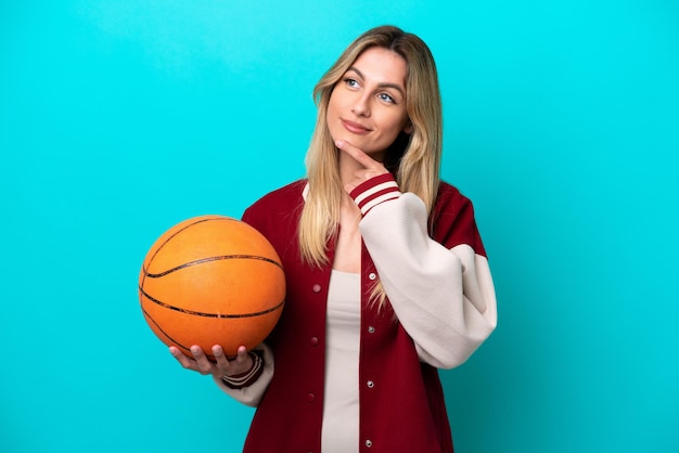 Giovane donna caucasica giocatore di basket isolata su sfondo blu e alzando lo sguardo