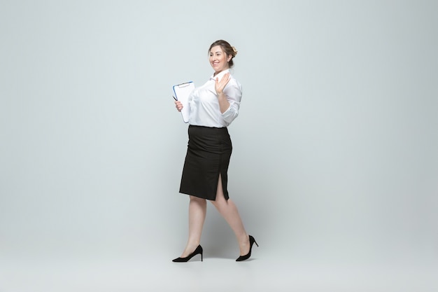 Giovane donna caucasica in abbigliamento casual su grigio. Personaggio femminile bodypositive, taglia forte