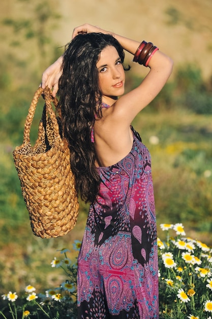 Giovane donna caucasica in abito fantasia viola con le braccia alzate e la borsa in testa