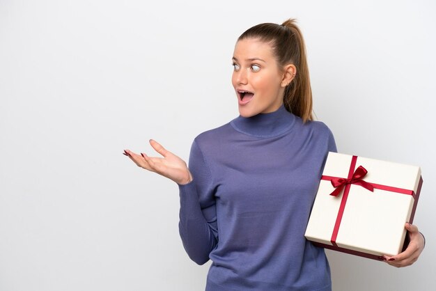 Giovane donna caucasica in possesso di un regalo isolato su sfondo bianco con espressione facciale a sorpresa