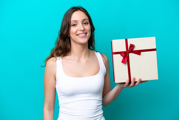 Giovane donna caucasica in possesso di un regalo isolato su sfondo blu sorridente molto