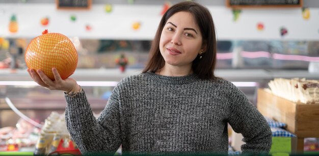 Giovane donna caucasica in un supermercato acquista verdure Tiene un pomelo nelle sue mani Concetto di acquisto di agrumi