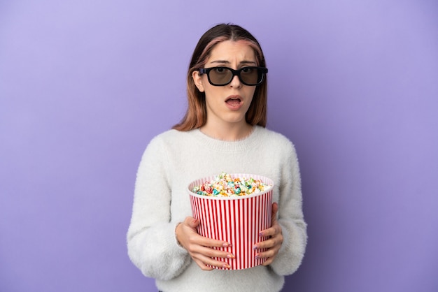 Giovane donna caucasica isolata con occhiali 3d e con in mano un grande secchio di popcorn