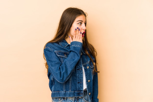 Giovane donna caucasica isolata su beige che è colpita a causa di qualcosa che ha visto.