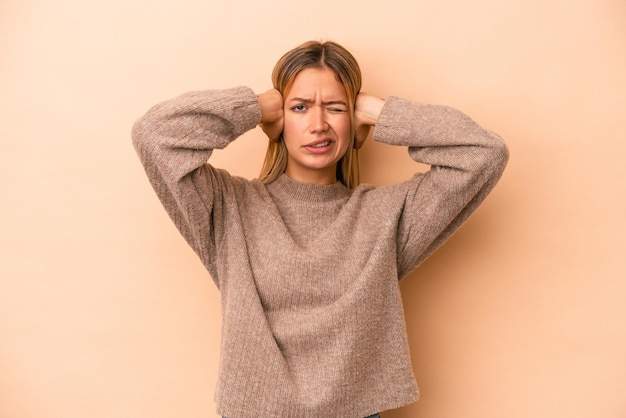 Giovane donna caucasica isolata su fondo beige che copre le orecchie con le mani.