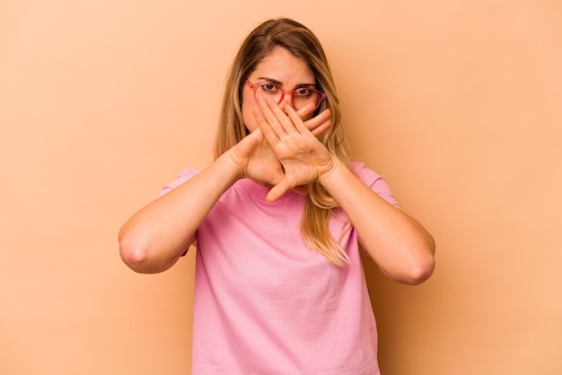 Giovane donna caucasica isolata su fondo beige che fa un gesto di rifiuto