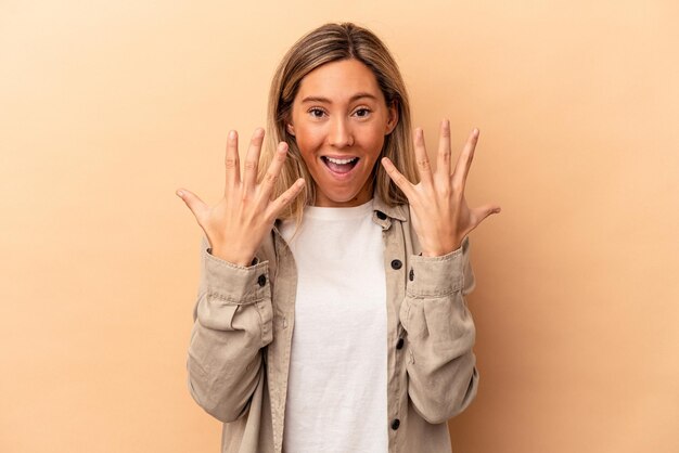 Giovane donna caucasica isolata su fondo beige che mostra il numero dieci con le mani.