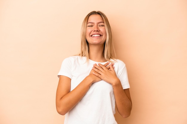 Giovane donna caucasica isolata su fondo beige che ride tenendo le mani sul cuore, concetto di felicità.