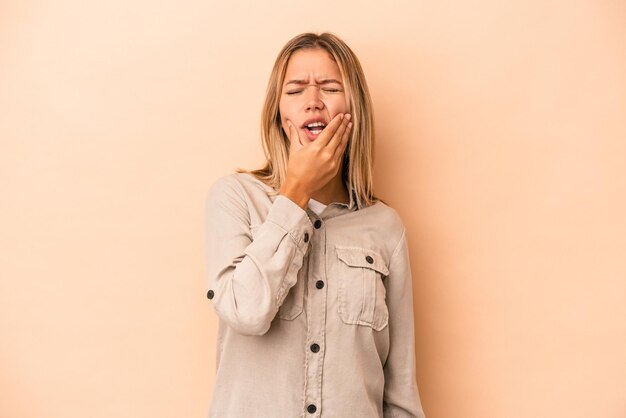 Giovane donna caucasica isolata su fondo beige con un forte dolore ai denti, dolore molare.