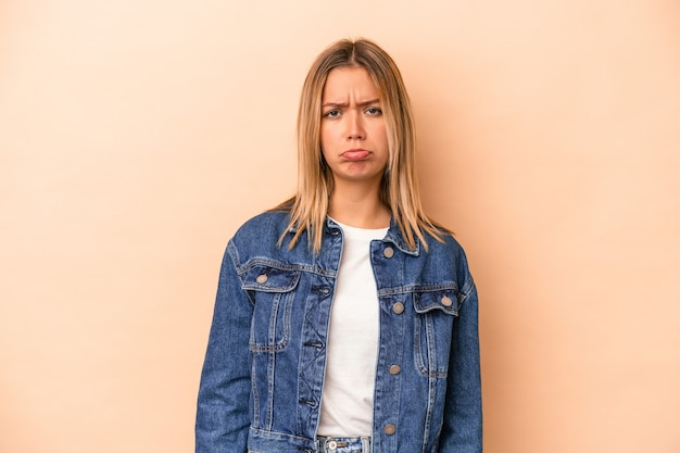 Giovane donna caucasica isolata su fondo beige faccia triste e seria, sentendosi miserabile e dispiaciuta.