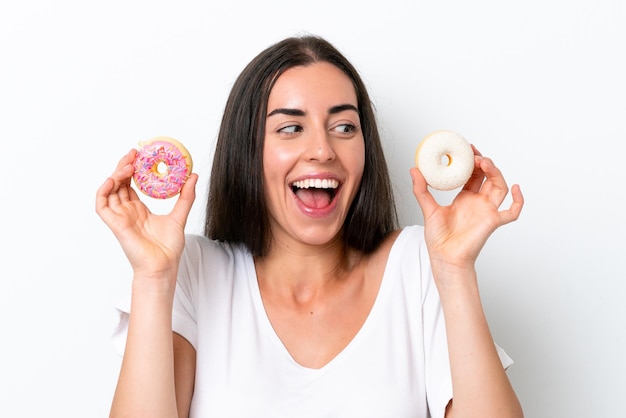 Giovane donna caucasica isolata su fondo bianco che tiene le ciambelle e sorpresa