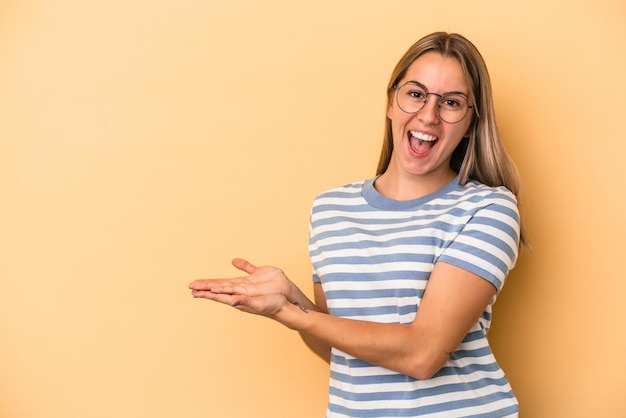 Giovane donna caucasica isolata su fondo giallo che tiene uno spazio della copia su una palma.