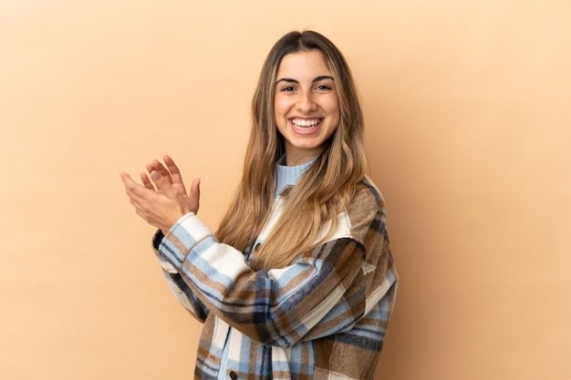 Giovane donna caucasica isolata su sfondo beige che applaude