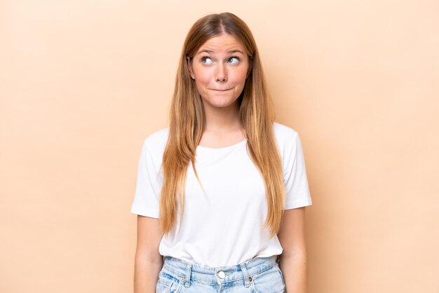 Giovane donna caucasica isolata su sfondo beige che ha dubbi mentre alza lo sguardo