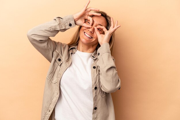 Giovane donna caucasica isolata su sfondo beige che mostra bene il segno sugli occhi