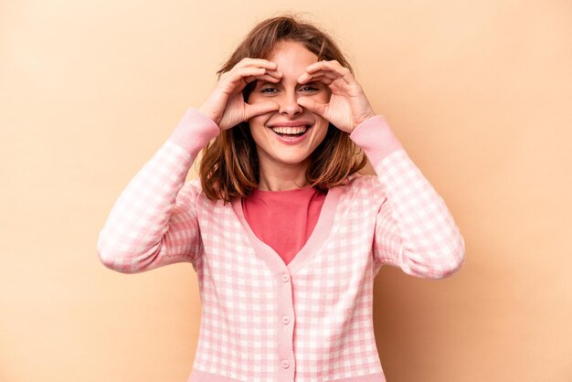 Giovane donna caucasica isolata su sfondo beige che mostra bene il segno sugli occhi