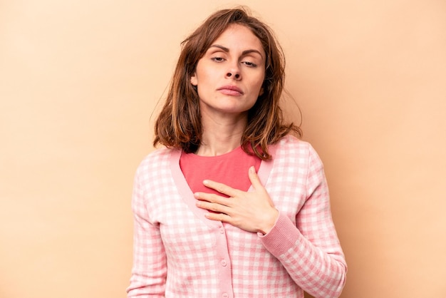 Giovane donna caucasica isolata su sfondo beige che presta giuramento mettendo la mano sul petto