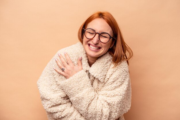 Giovane donna caucasica isolata su sfondo beige che ride e si diverte.