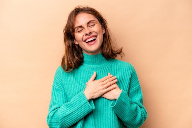 Giovane donna caucasica isolata su sfondo beige che ride tenendo le mani sul concetto di felicità del cuore