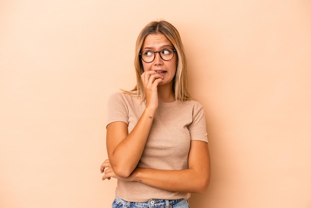 Giovane donna caucasica isolata su sfondo beige che si morde le unghie, nervosa e molto ansiosa.