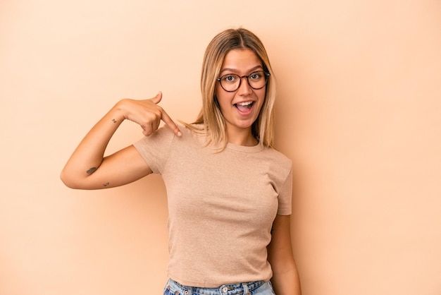 Giovane donna caucasica isolata su sfondo beige persona che indica a mano uno spazio copia camicia, orgogliosa e fiduciosa