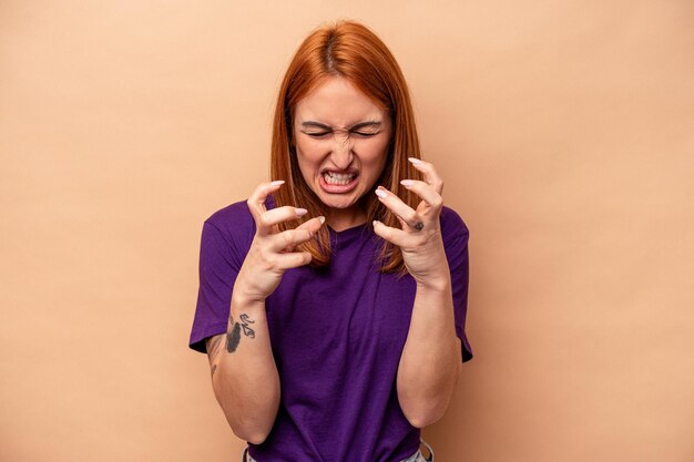 Giovane donna caucasica isolata su sfondo beige sconvolta urlando con le mani tese.