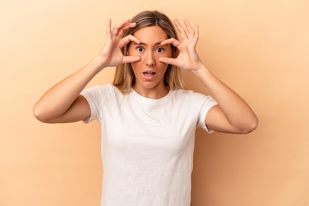 Giovane donna caucasica isolata su sfondo beige tenendo gli occhi aperti per trovare un'opportunità di successo.