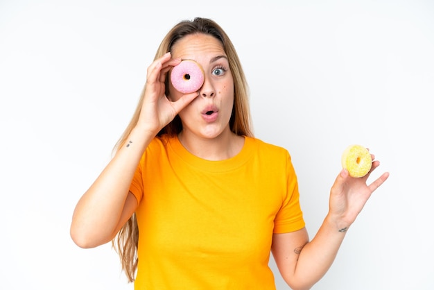 Giovane donna caucasica isolata su sfondo bianco che tiene una ciambella in un occhio