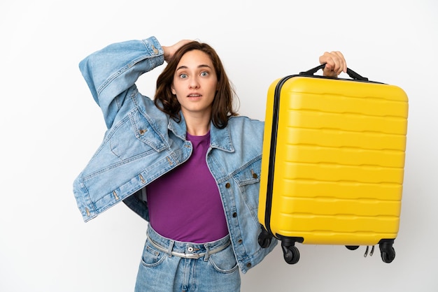 Giovane donna caucasica isolata su sfondo bianco in vacanza con valigia da viaggio e sorpresa