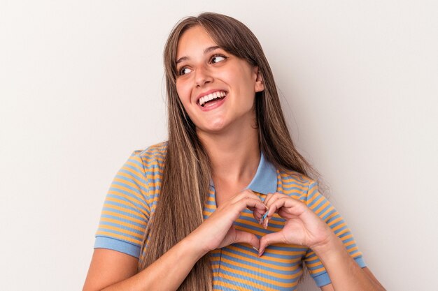 Giovane donna caucasica isolata su sfondo bianco sorridente e mostrando una forma di cuore con le mani.