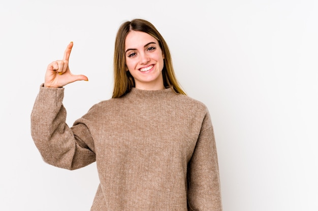 Giovane donna caucasica isolata su sfondo bianco tenendo qualcosa di poco con gli indici, sorridente e fiducioso.