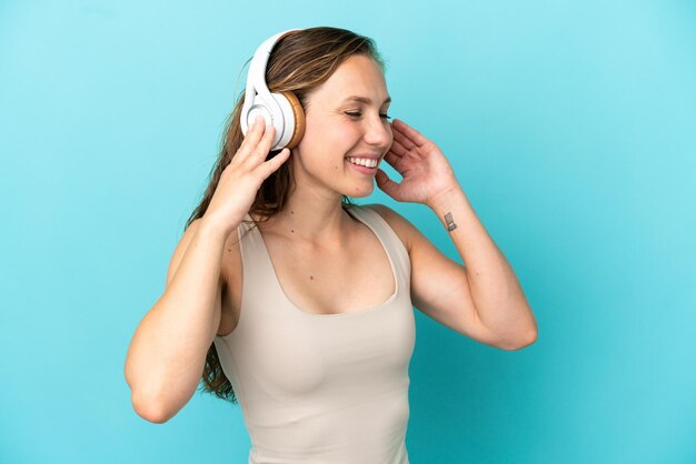 Giovane donna caucasica isolata su sfondo blu ascoltando musica e cantando