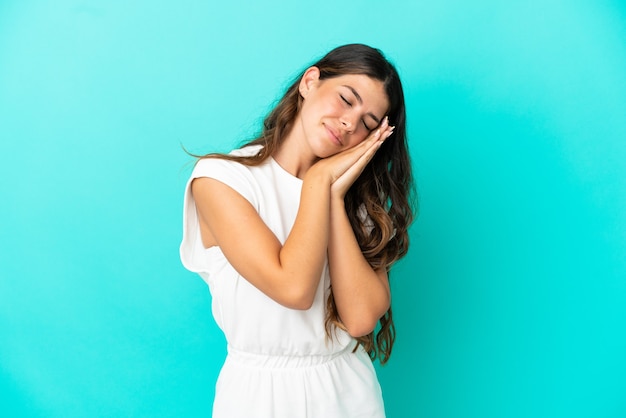 Giovane donna caucasica isolata su sfondo blu che fa il gesto del sonno in un'espressione adorabile