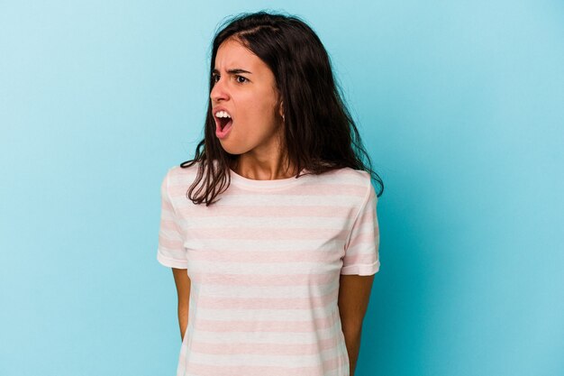 Giovane donna caucasica isolata su sfondo blu che grida molto arrabbiato, concetto di rabbia, frustrato.